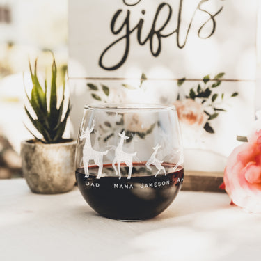 Etched stemless red wine glass. The etching wraps around the glass. The design is of a family of deer lined in a row. There is a dad deer, mom deer and three kids. Under each deer has a printed name "Dad, Mama, Jameson, Anya, Brian". Deer can be added or taken away.